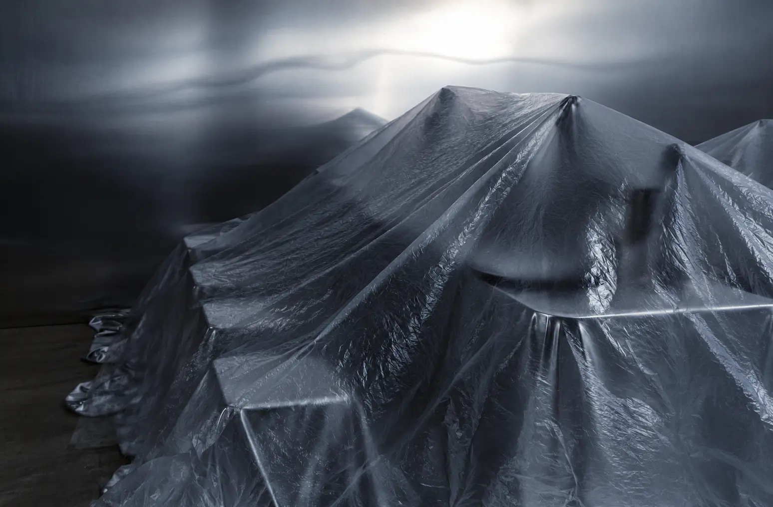 Abstract sculptural installation covered in reflective silver fabric, featuring dramatic folds and atmospheric lighting.