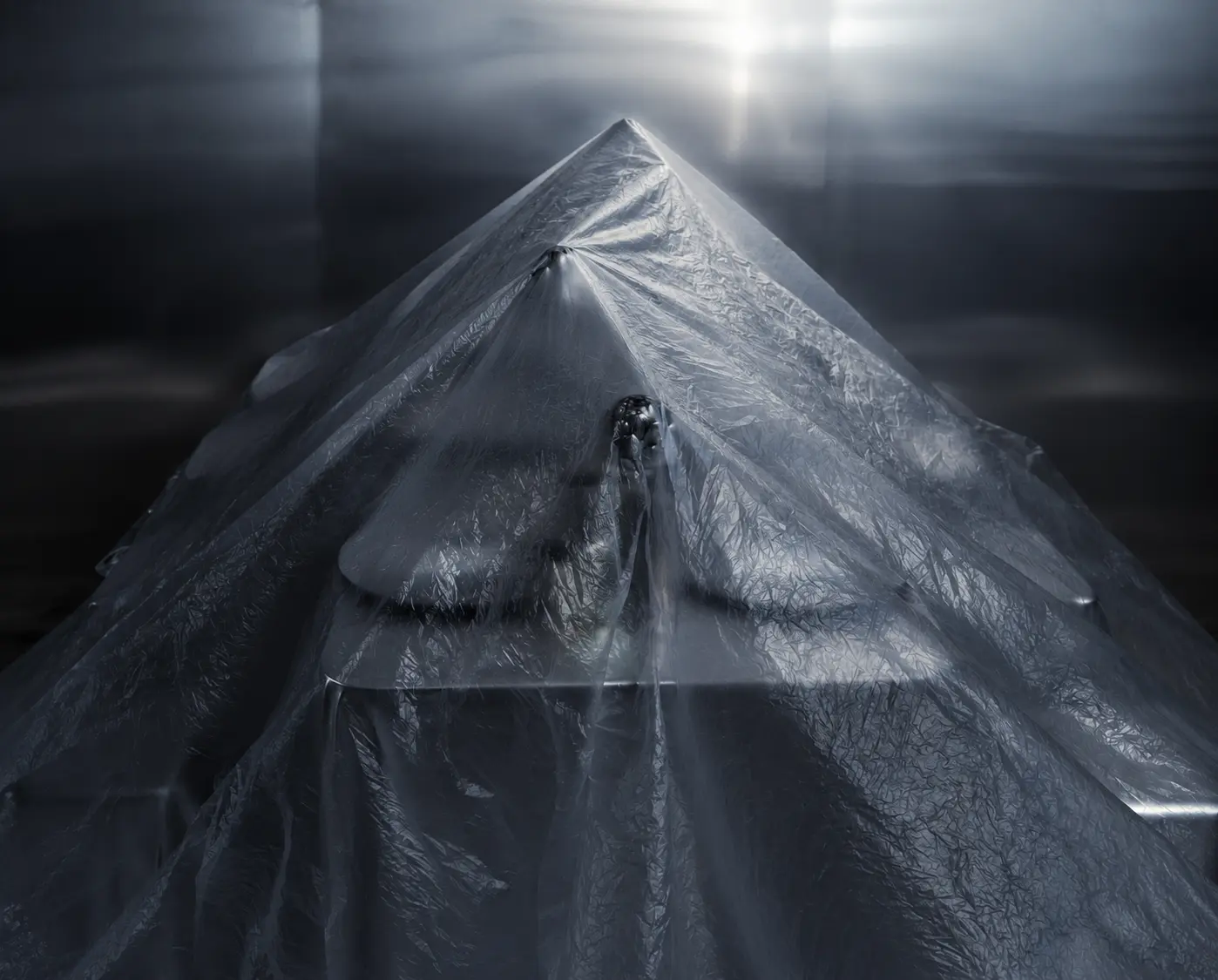 Geometric sculptural installation draped in reflective silver fabric, forming a dramatic triangular silhouette under soft overhead lighting.