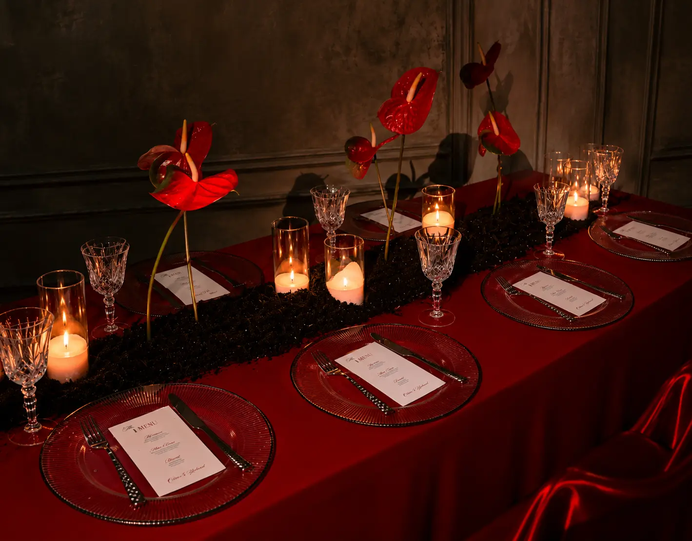 Elevated view of a red editorial dining table with sculptural red anthuriums, black floral centerpiece, crystal glasses, candles and personalized menus.