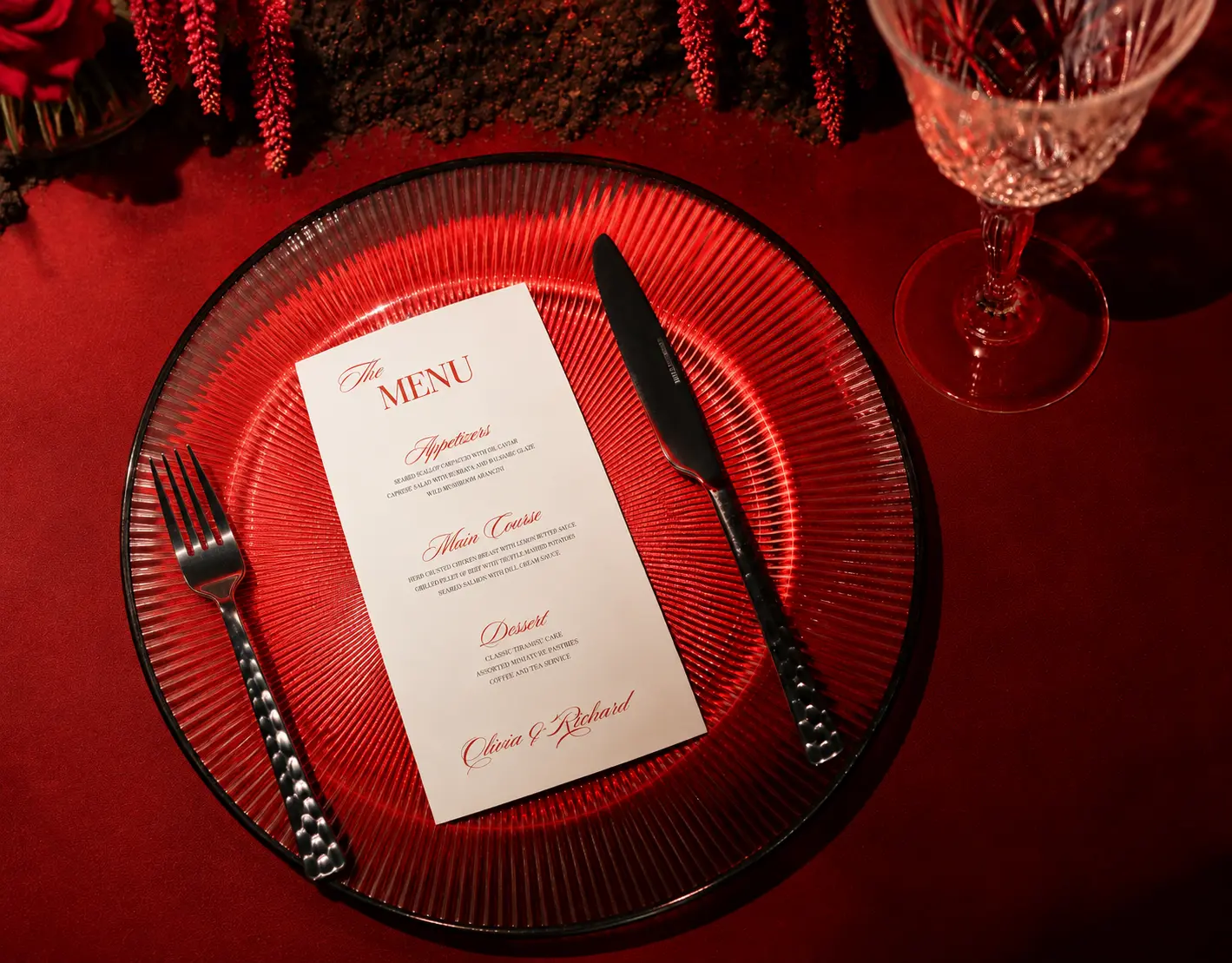 Overhead view of an elegant red wedding place setting with a personalized menu, ribbed red glass plate, silver cutlery and crystal wine glass.