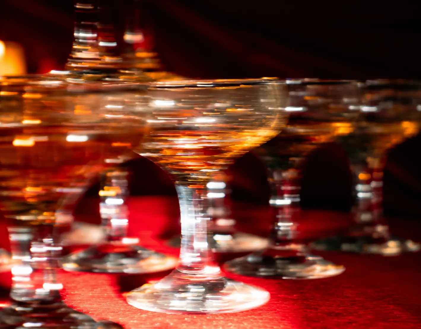 Close-up of champagne coupe glasses arranged on rich red fabric, reflecting warm golden light in an editorial event setting.