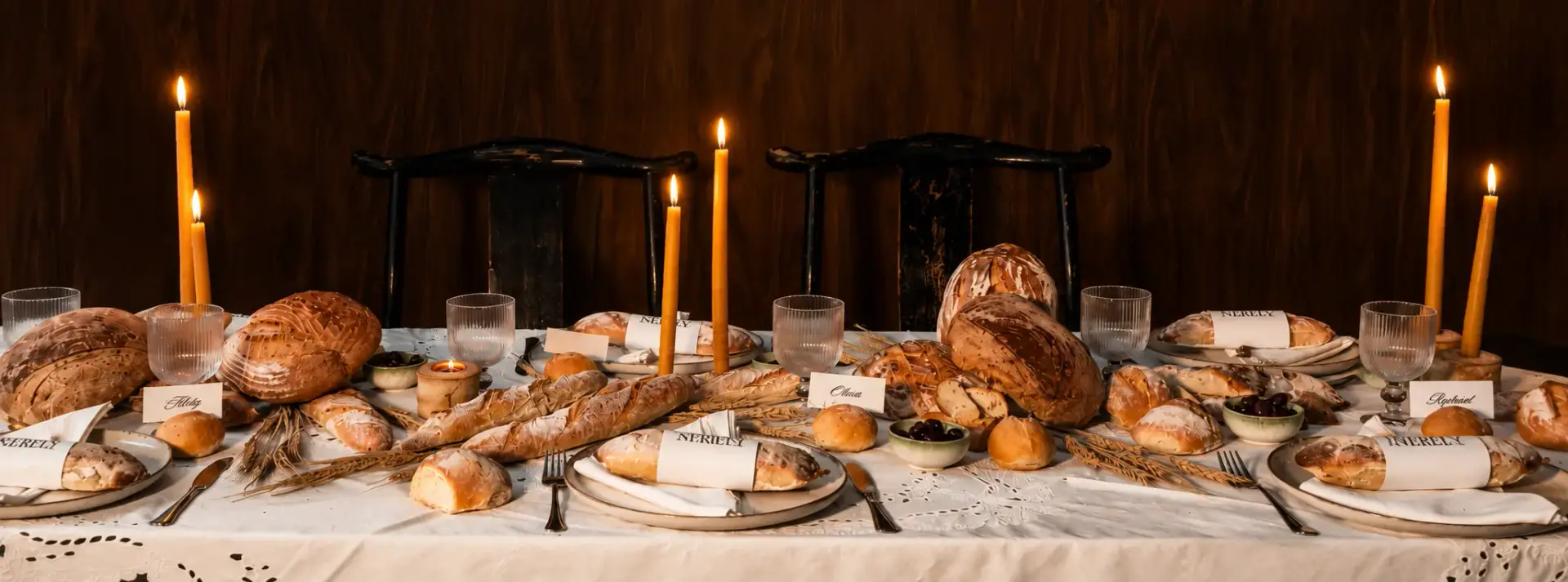LEVEIN brand experience tablescape featuring artisan bread, rustic tableware, embroidered linens and tall lit candles.