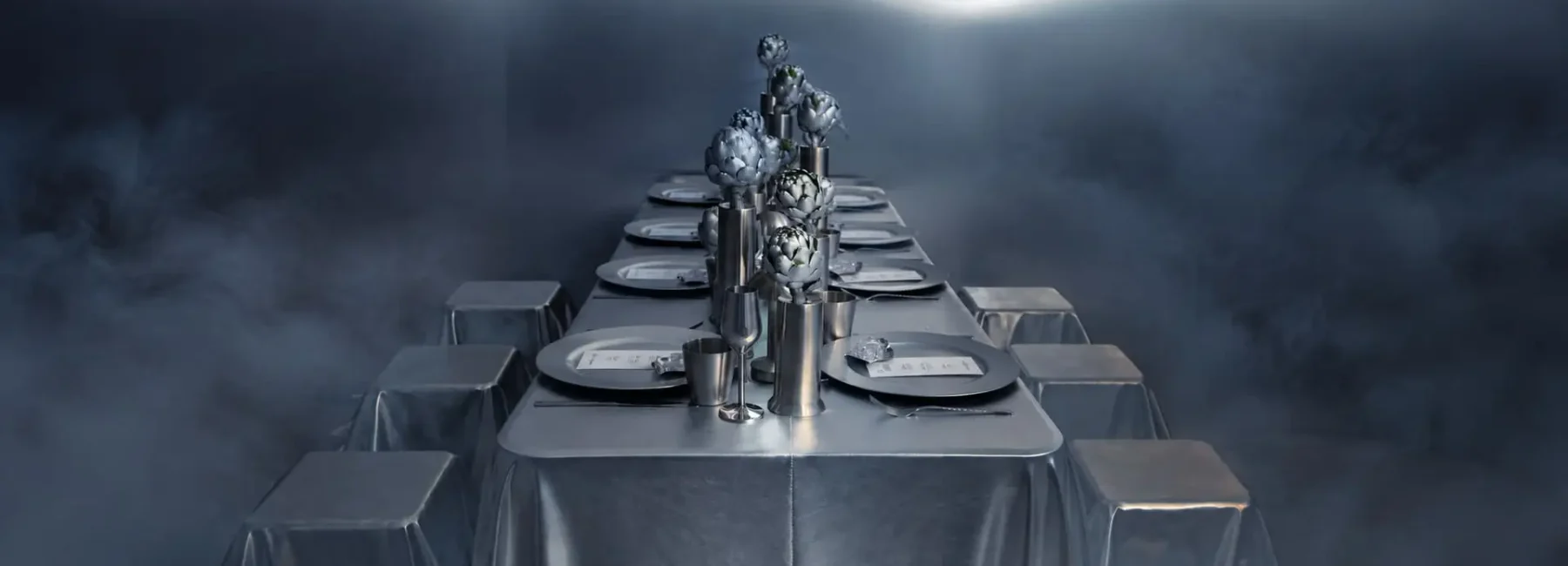 Contemporary event tablescape with metallic silver linens, artichoke centerpieces and sculptural seating surrounded by atmospheric mist.