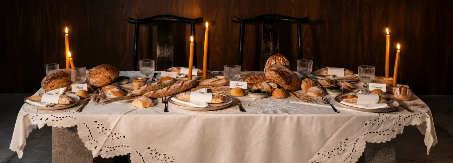 Rustic tablescape featuring artisan bread, lit taper candles, vintage tableware and an embroidered white tablecloth.