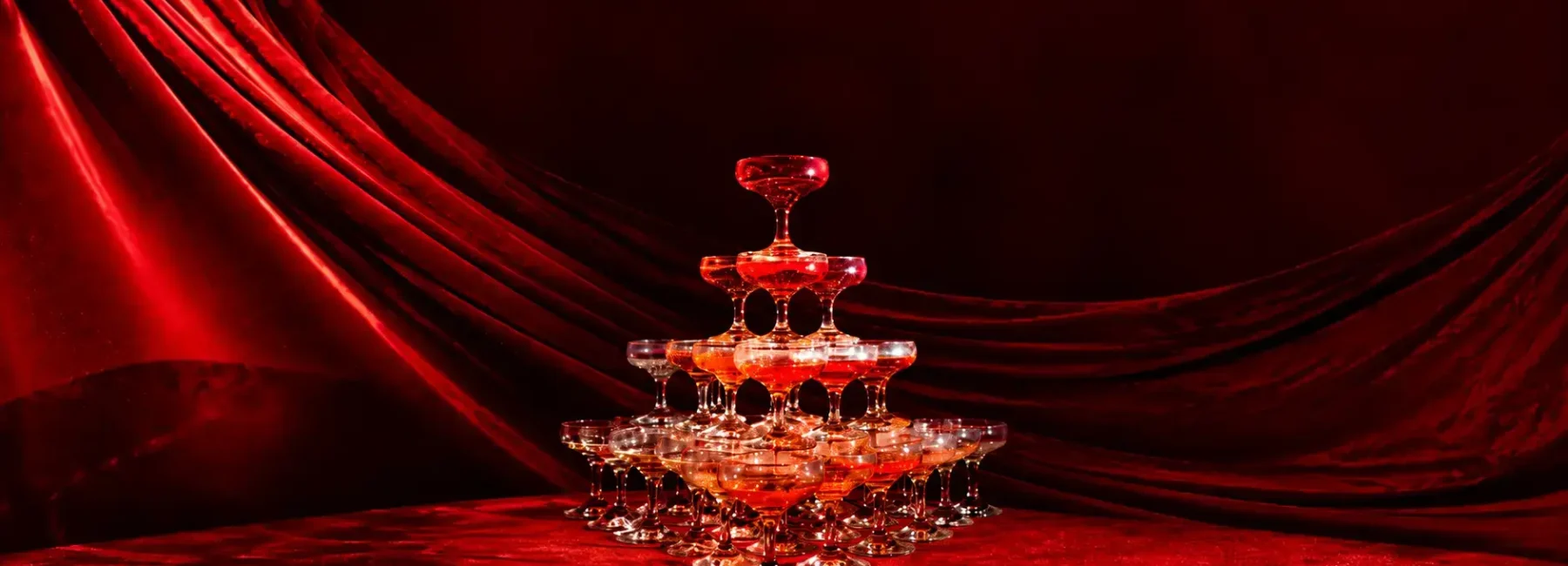 Champagne tower arranged against a dramatic red velvet backdrop with rich red lighting.